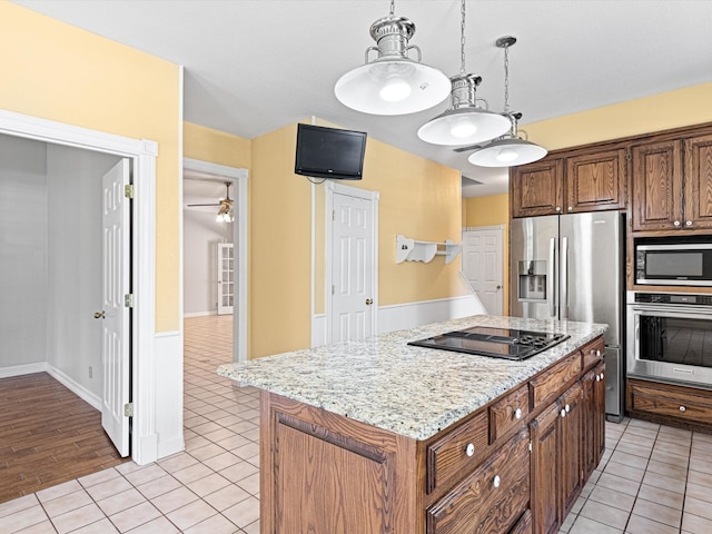 kitchen with appliances with stainless steel finishes, a center island, hanging light fixtures, and light tile patterned flooring