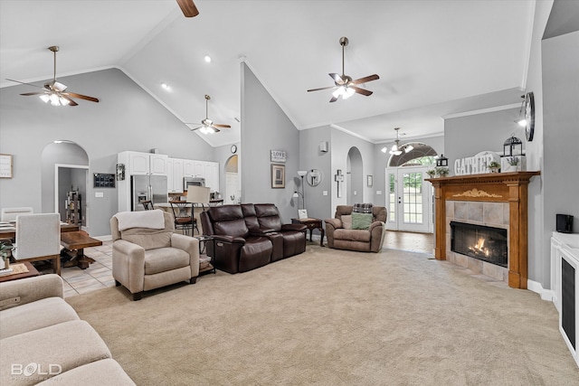 carpeted living room featuring high vaulted ceiling, ceiling fan with notable chandelier, ornamental molding, and a tile fireplace