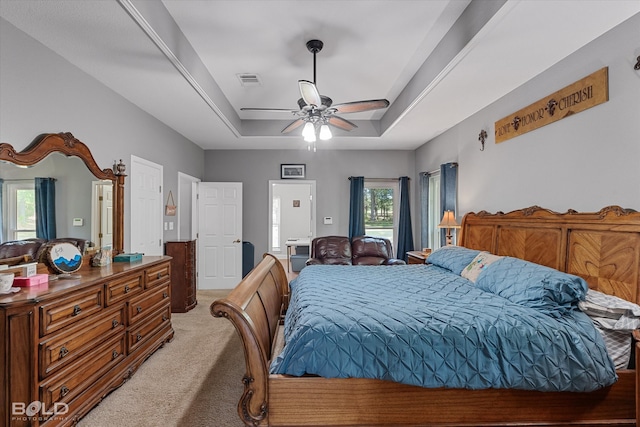 bedroom with carpet, a tray ceiling, multiple windows, and ceiling fan