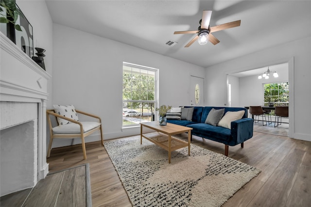 living room with a wealth of natural light, ceiling fan with notable chandelier, and light hardwood / wood-style floors