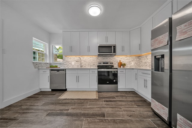 kitchen with dark hardwood / wood-style floors, appliances with stainless steel finishes, tasteful backsplash, sink, and white cabinetry