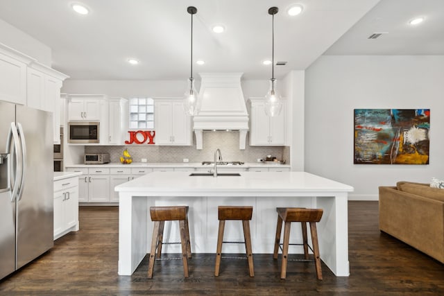 kitchen with stainless steel refrigerator with ice dispenser, built in microwave, pendant lighting, and an island with sink