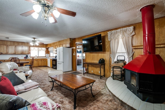 tiled living room with ceiling fan, a wood stove, wood walls, and a textured ceiling