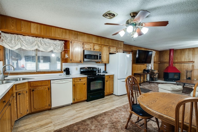 kitchen featuring white appliances, a textured ceiling, sink, a wood stove, and wood walls