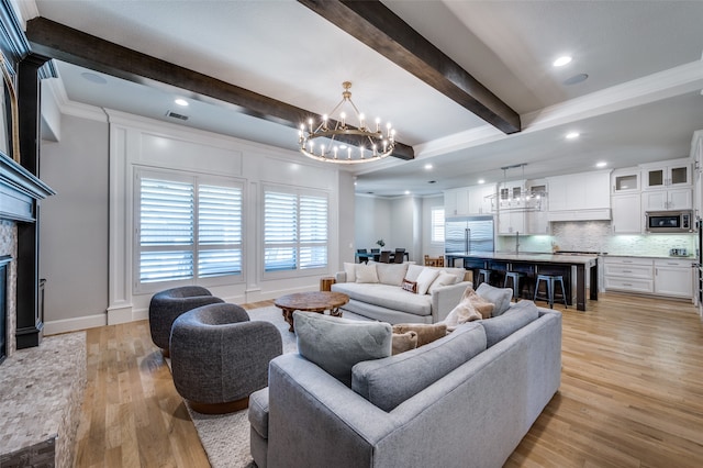 living room featuring beamed ceiling, a stone fireplace, light wood-type flooring, and a chandelier