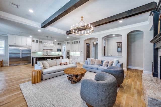 living room featuring light wood-type flooring, a notable chandelier, crown molding, and beamed ceiling