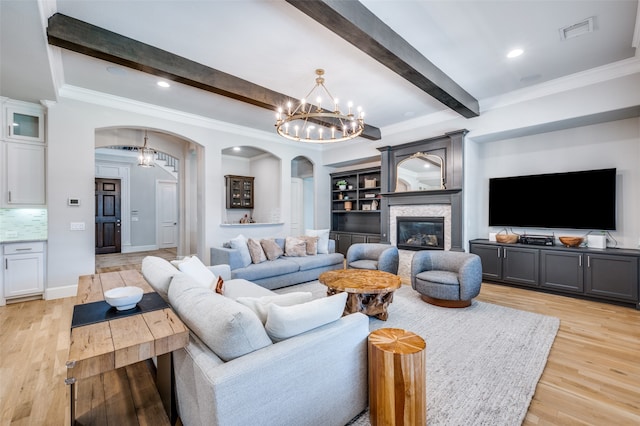 living room with crown molding, light hardwood / wood-style flooring, a notable chandelier, beamed ceiling, and a stone fireplace