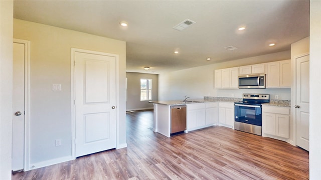 kitchen with white cabinets, sink, kitchen peninsula, appliances with stainless steel finishes, and light hardwood / wood-style floors