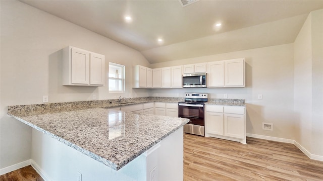 kitchen with kitchen peninsula, lofted ceiling, stainless steel appliances, and white cabinets