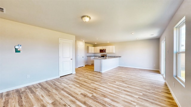 kitchen with kitchen peninsula, light wood-type flooring, a healthy amount of sunlight, and white cabinetry