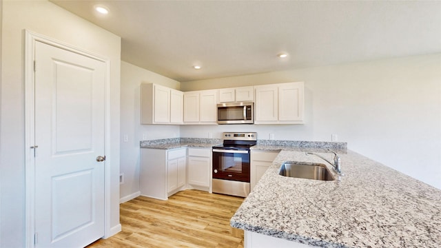 kitchen featuring light wood-type flooring, sink, kitchen peninsula, appliances with stainless steel finishes, and white cabinetry