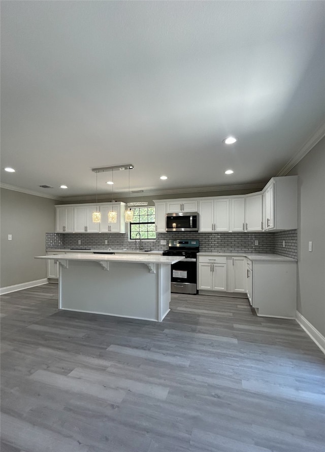 kitchen with appliances with stainless steel finishes, hardwood / wood-style floors, pendant lighting, white cabinets, and a kitchen breakfast bar