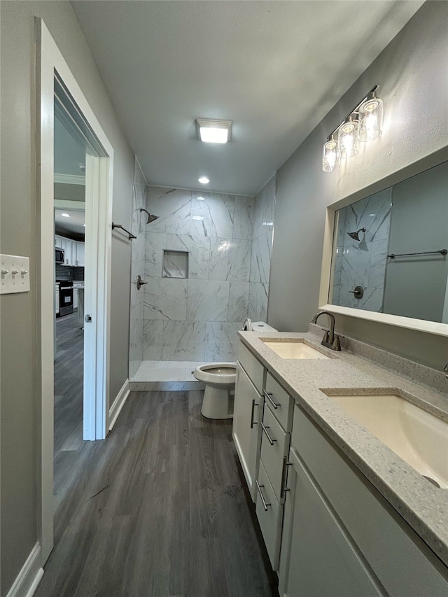 bathroom with toilet, a tile shower, hardwood / wood-style floors, and vanity