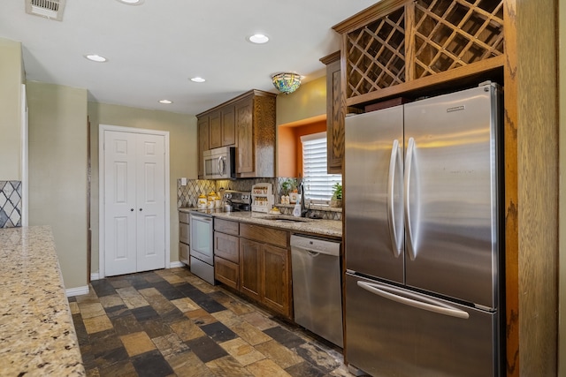 kitchen with stainless steel appliances, dark tile patterned floors, decorative backsplash, sink, and light stone counters