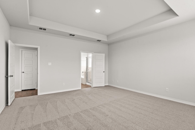 unfurnished bedroom featuring ensuite bath, a raised ceiling, and carpet