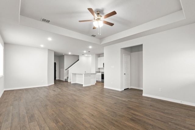 unfurnished living room featuring dark hardwood / wood-style floors, a raised ceiling, and ceiling fan