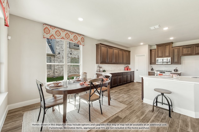 kitchen with a kitchen breakfast bar, stainless steel appliances, light hardwood / wood-style flooring, and decorative backsplash