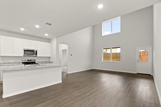 kitchen with white cabinetry, stainless steel appliances, dark hardwood / wood-style floors, light stone countertops, and a center island with sink