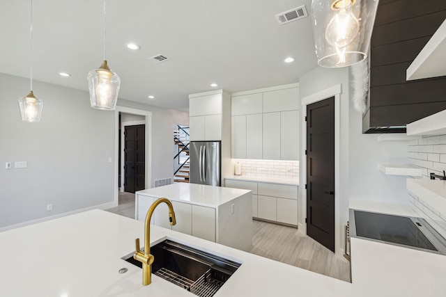 kitchen with light wood-type flooring, pendant lighting, tasteful backsplash, white cabinetry, and stainless steel fridge