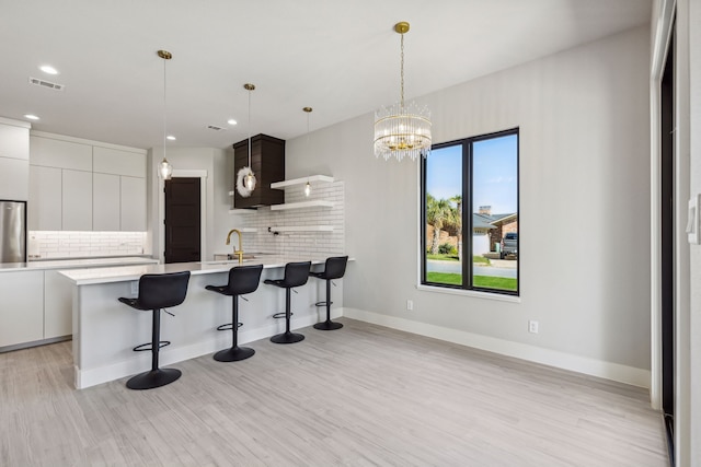 kitchen with light hardwood / wood-style floors, decorative backsplash, refrigerator, white cabinets, and a kitchen breakfast bar