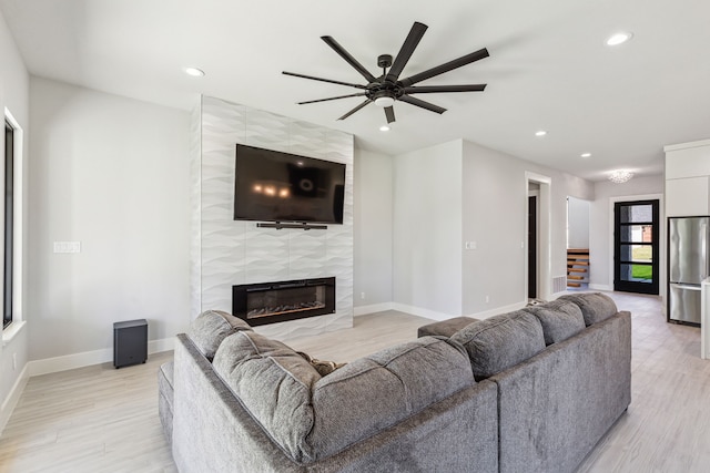 living room with ceiling fan, light wood-type flooring, and a tiled fireplace