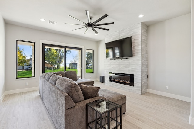 living room with ceiling fan, light hardwood / wood-style flooring, and a tiled fireplace