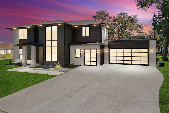 contemporary home with a balcony, a yard, and a garage