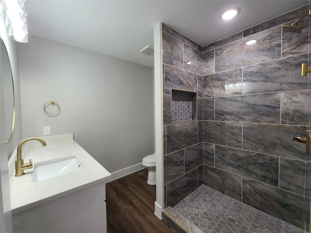 bathroom with wood-type flooring, vanity, a tile shower, and toilet