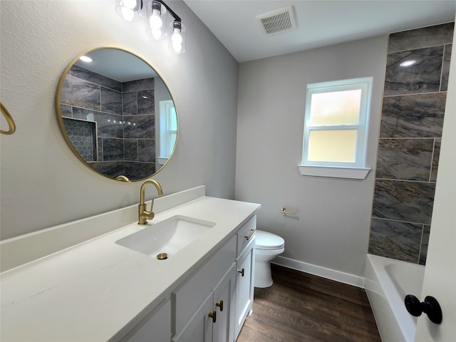 full bathroom with wood-type flooring, tiled shower / bath, vanity, and toilet