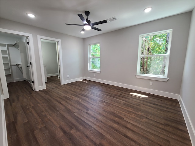 unfurnished bedroom with ceiling fan, a closet, dark wood-type flooring, and a walk in closet