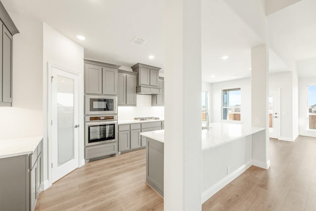 kitchen with appliances with stainless steel finishes, gray cabinetry, and light hardwood / wood-style flooring