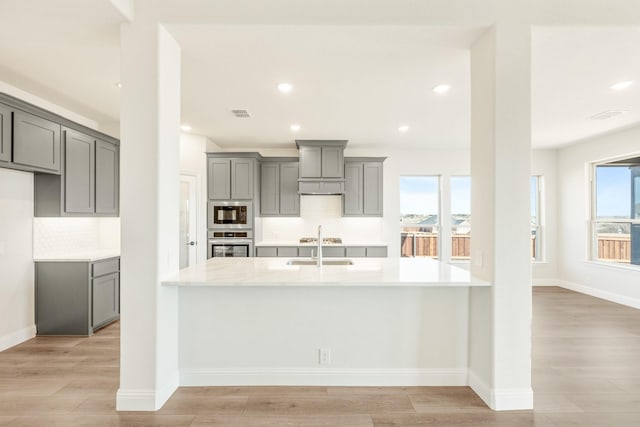 kitchen with light wood-type flooring, stainless steel appliances, light stone countertops, sink, and gray cabinets