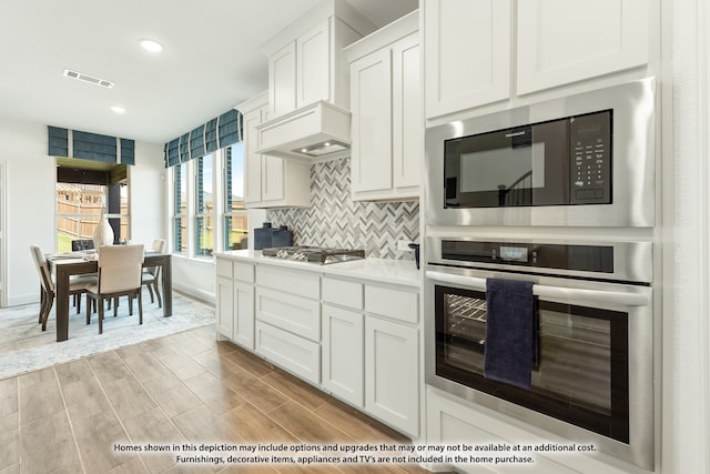 kitchen featuring backsplash, light hardwood / wood-style floors, premium range hood, stainless steel appliances, and white cabinets