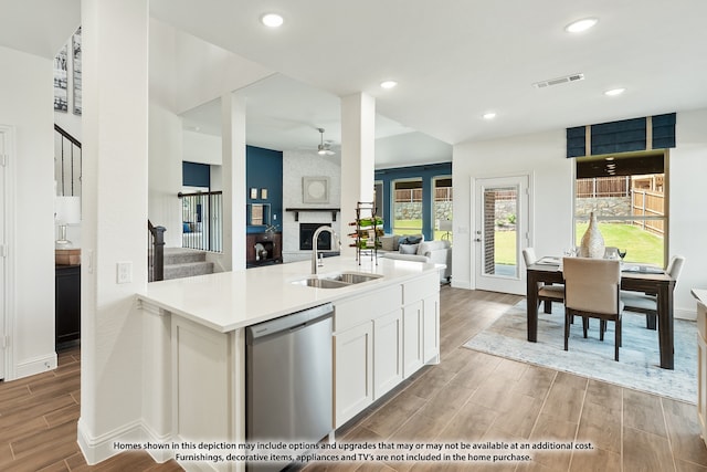 kitchen featuring dishwasher, light hardwood / wood-style floors, sink, white cabinets, and a brick fireplace