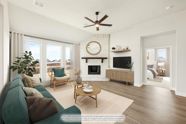 living room featuring ceiling fan, a stone fireplace, vaulted ceiling, and hardwood / wood-style floors