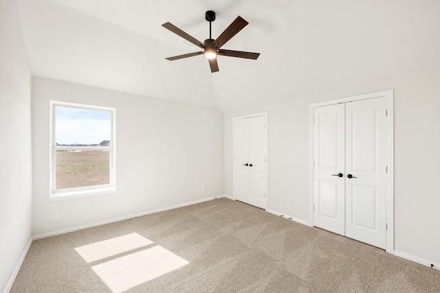 unfurnished bedroom with ceiling fan, multiple closets, vaulted ceiling, and light carpet