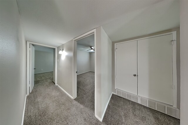 hallway featuring a textured ceiling, carpet flooring, and baseboards