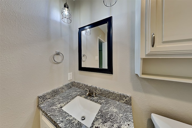 bathroom featuring toilet, a textured wall, and vanity