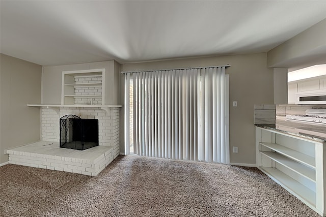 unfurnished living room with carpet floors, a brick fireplace, built in shelves, and baseboards