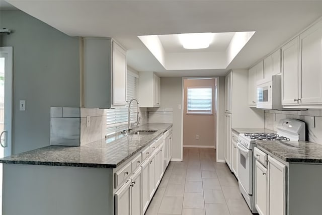 kitchen with a tray ceiling, tasteful backsplash, a sink, white appliances, and baseboards