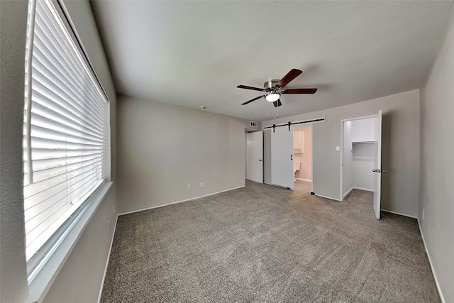 unfurnished bedroom with ceiling fan, a spacious closet, a barn door, and carpet