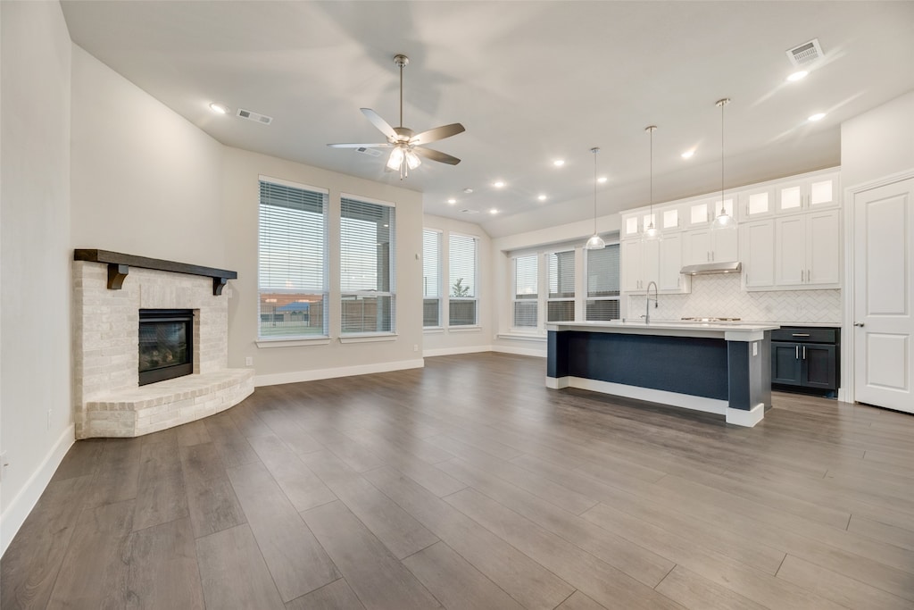 unfurnished living room featuring ceiling fan, visible vents, a fireplace, and wood finished floors