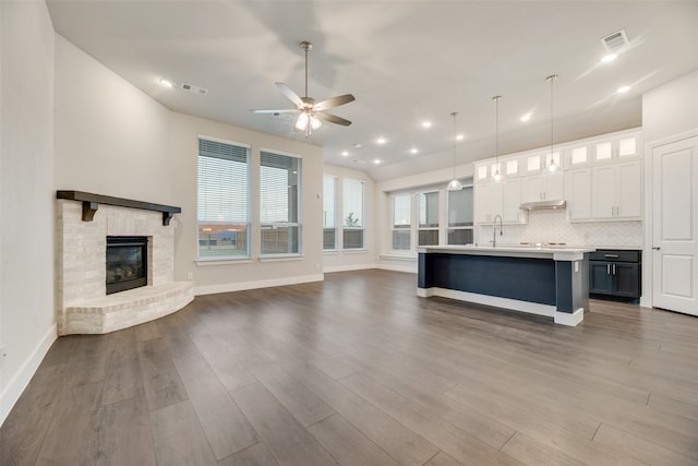 unfurnished living room featuring a brick fireplace, sink, wood-type flooring, and ceiling fan