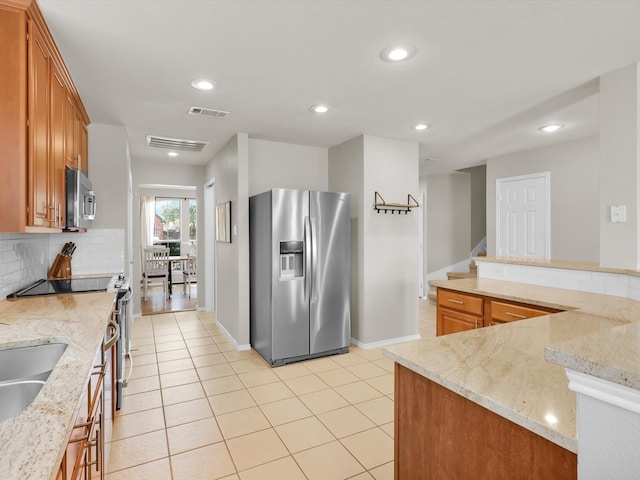 kitchen featuring backsplash, light stone countertops, light tile patterned floors, stainless steel appliances, and kitchen peninsula