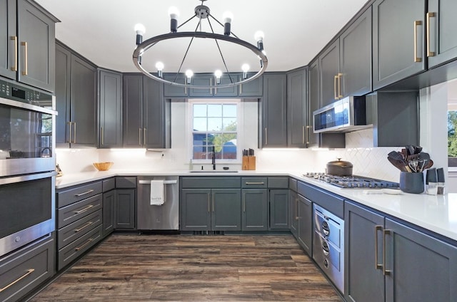 kitchen featuring hanging light fixtures, stainless steel appliances, a chandelier, gray cabinets, and dark wood-type flooring