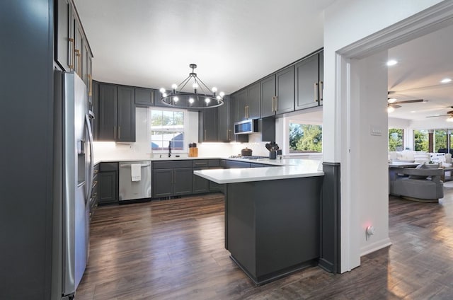 kitchen featuring ceiling fan with notable chandelier, dark hardwood / wood-style flooring, pendant lighting, appliances with stainless steel finishes, and kitchen peninsula