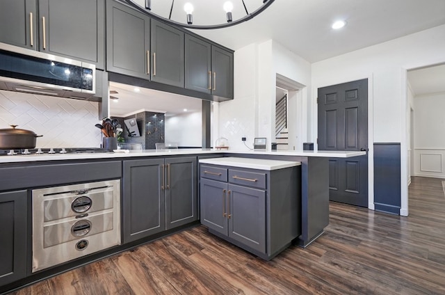 kitchen with gray cabinetry, an inviting chandelier, dark hardwood / wood-style flooring, tasteful backsplash, and kitchen peninsula