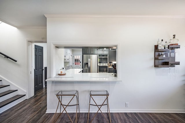 kitchen featuring dark hardwood / wood-style floors, stainless steel appliances, crown molding, and kitchen peninsula