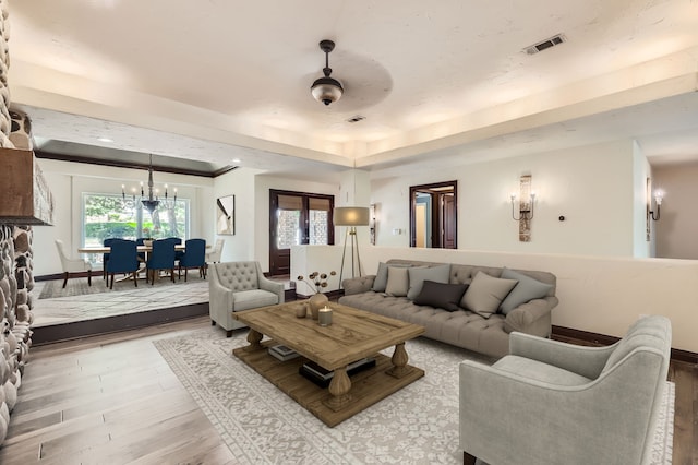 living room featuring ceiling fan with notable chandelier, light hardwood / wood-style floors, and a tray ceiling