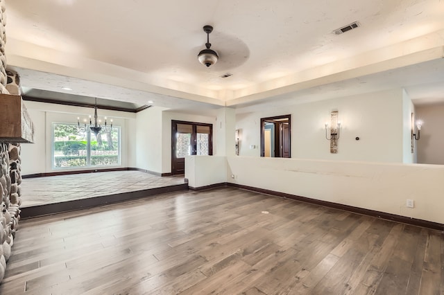 spare room featuring a raised ceiling, wood-type flooring, and ceiling fan with notable chandelier